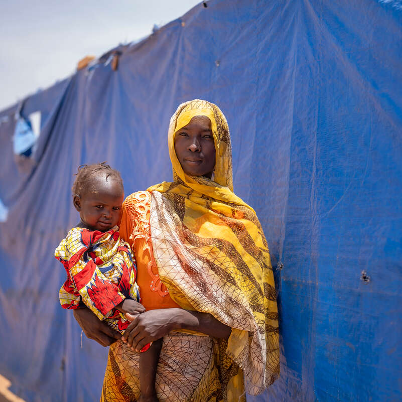 Malawiya, 27, är flykting från Sudan. Hon står med sin två år gamla dotter i armarna utanför ett av RESCUE:s hälsocenter i östra Chad.