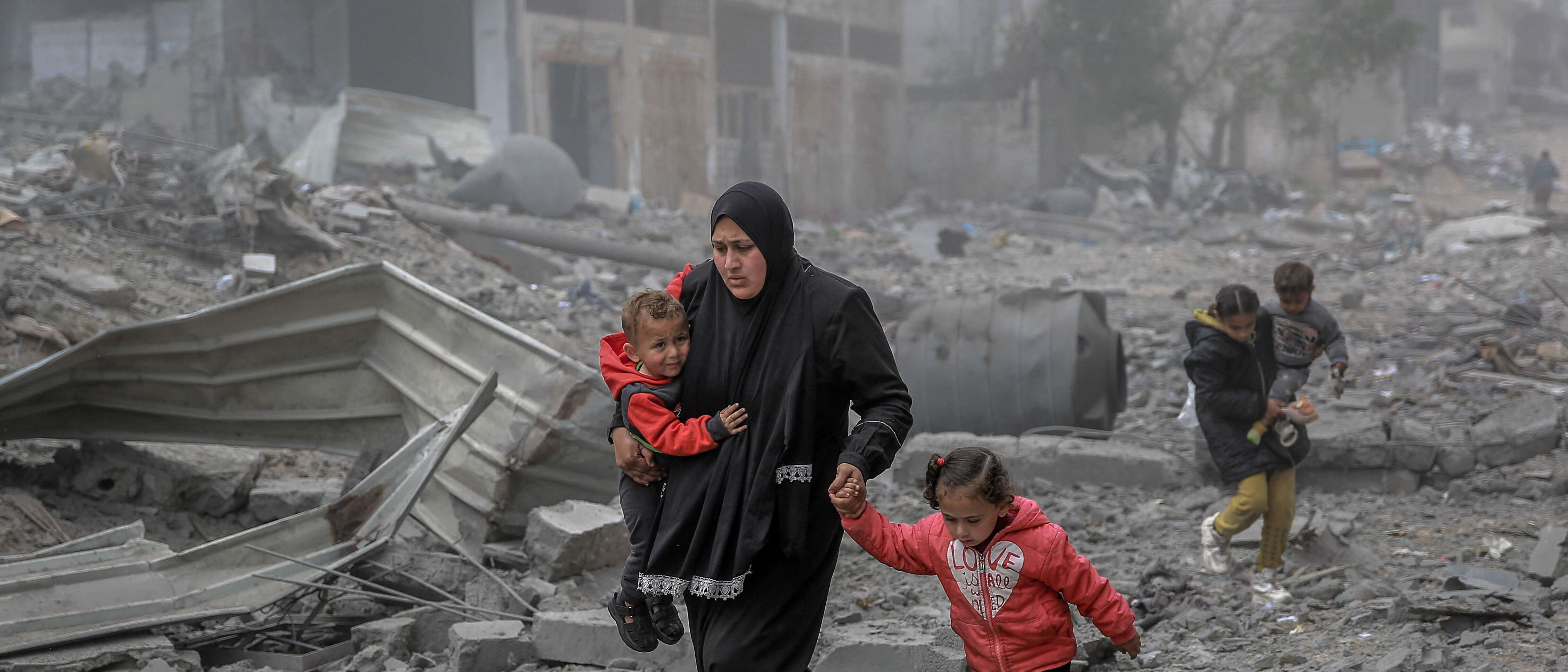 A mother holds her two children while she makes her way through the remnants of a building destroyed by the war in Gaza.