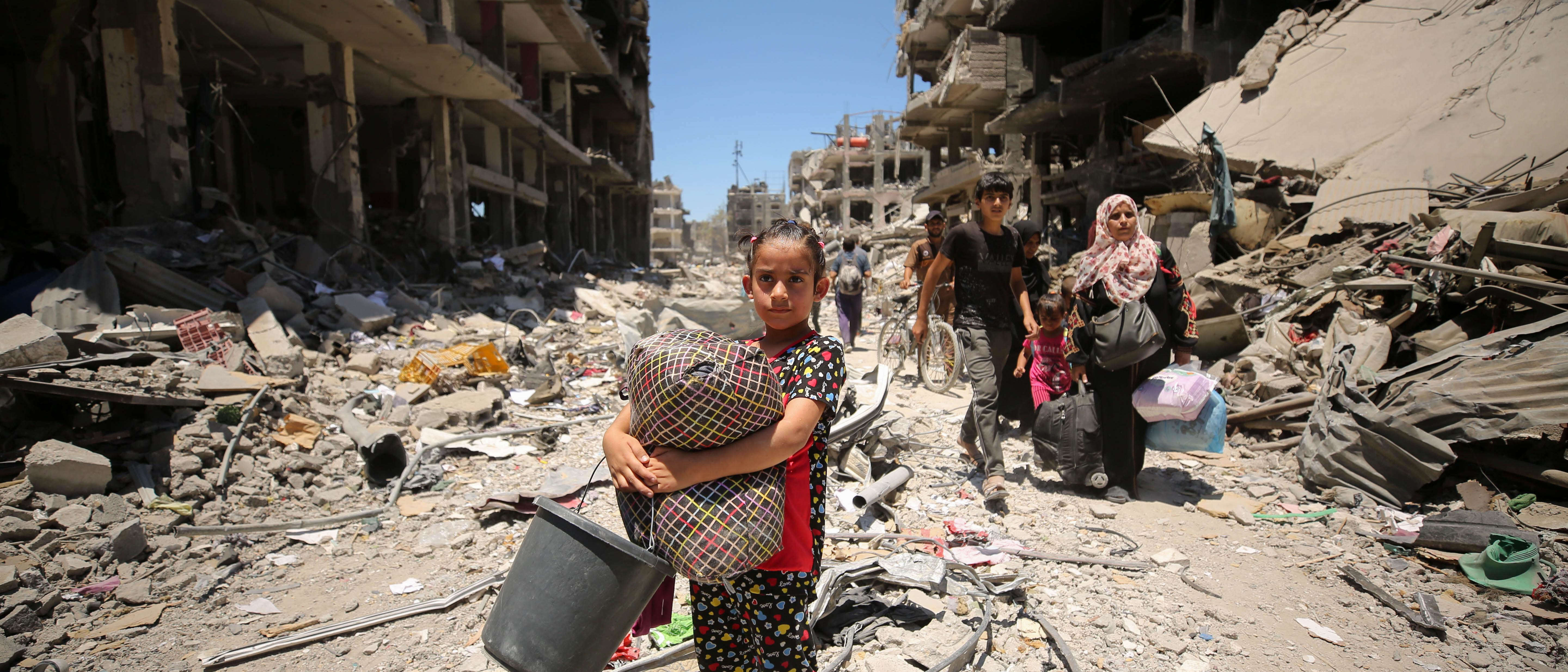 Young girl stands amongst rubble in Gaza.