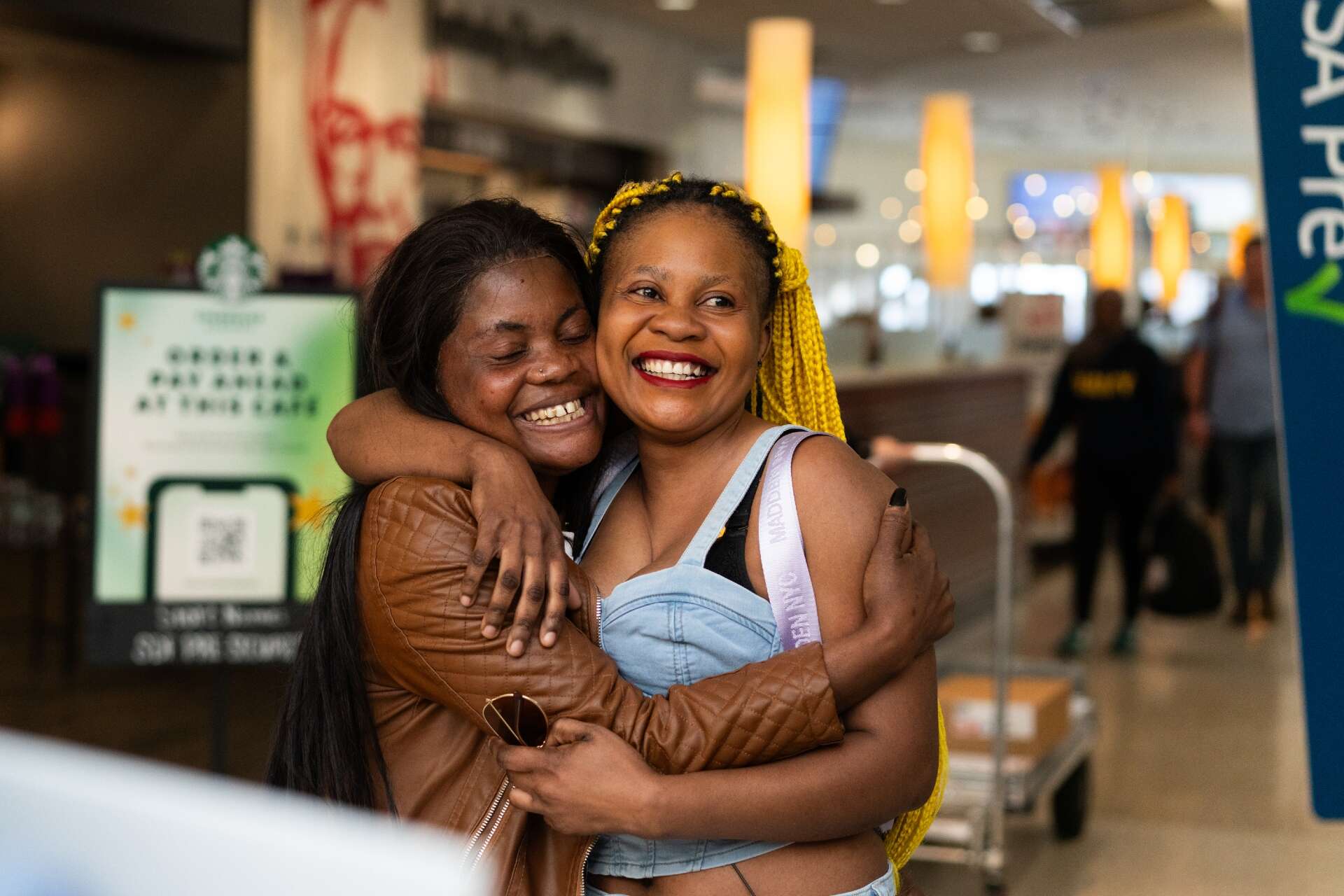 Two women stand and embrace after reunifying at an airport.