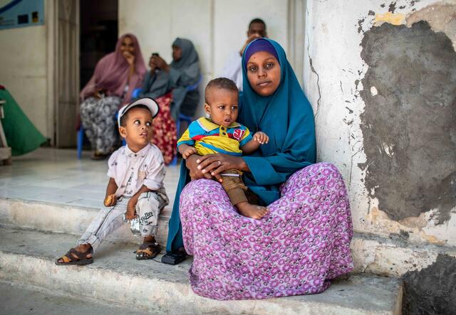 En mamma väntar med sina två barn och andra människor framför sjukhuset i Karaan i Somalia