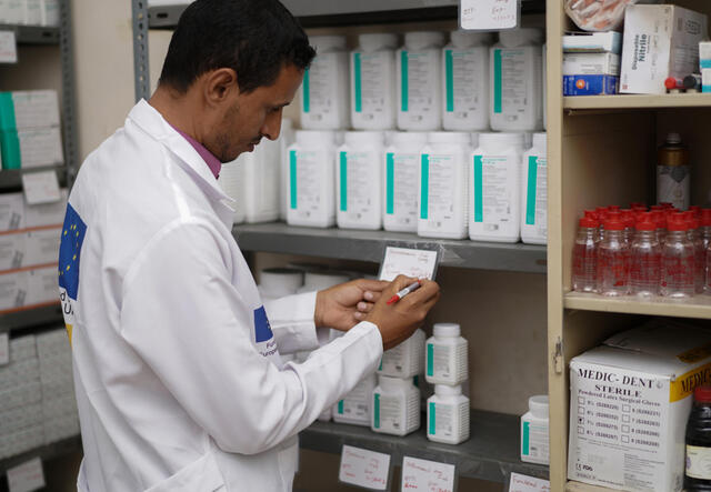 Doctor in white coat in store room making notes on inventory