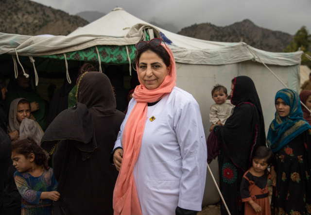 Dr. Naija stands in front of a tent and a group of women.