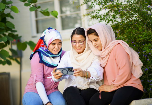 Arifa, Zahra and Hadisa sit together looking at a phone held by Zahra