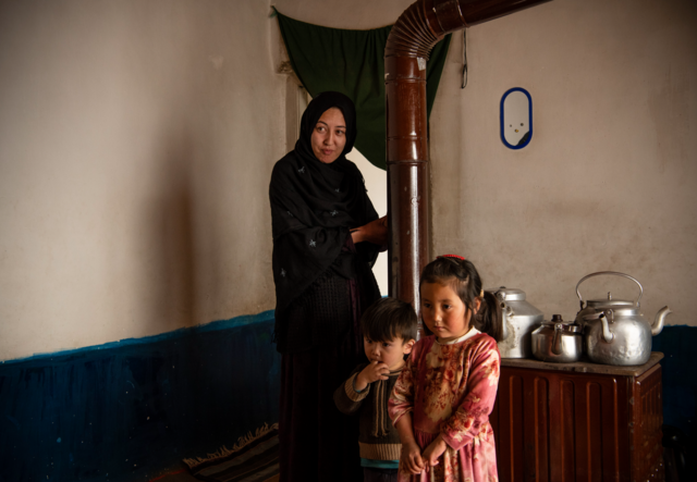 Aalia stands in her living room with two children in front of her.