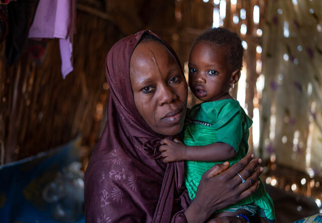 Fandaou holds her daughter while posing for a portrait taken in their houses, seemingly made of sticks and wood, in Niger.