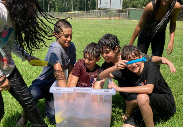 A group of summer camp students looking for water balloons in a small bin of water.