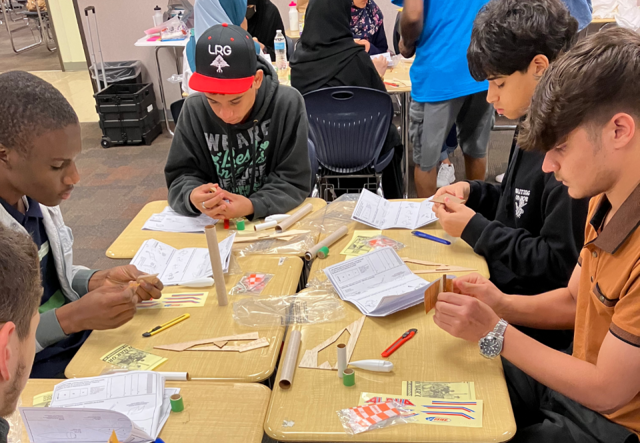 A group of 4 students gathered around a table working on bottle rockets.