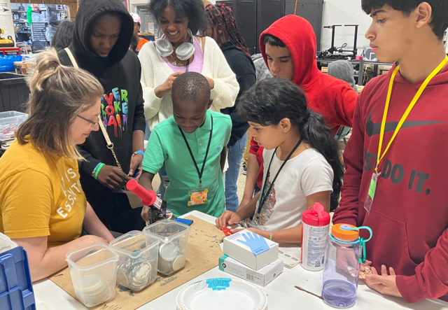 A group of middle school students gathered around a button maker.