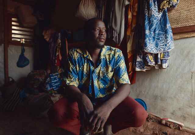 A man sits on the floor of a home and stares in the distance while posing for a portrait.