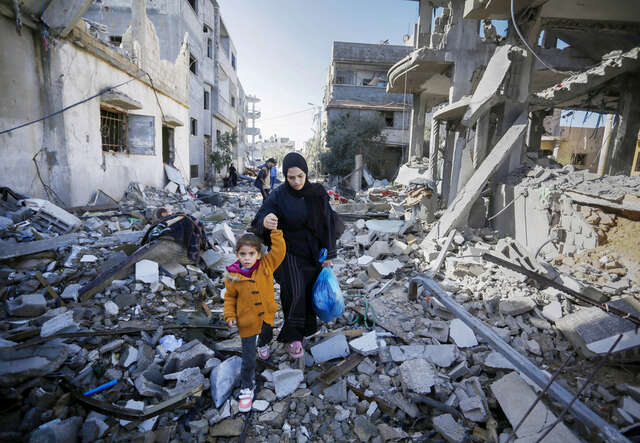 En mamma med sitt barn går över ruiner i Gaza. 