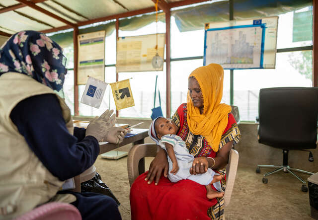 Almas holds her son Hermon while receiving vital support from an IRC nutrition specialist.