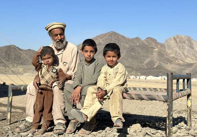 Ein Mann und seine drei Söhne posieren für ein Foto, während sie auf einem Feldbett in der Wüste sitzen