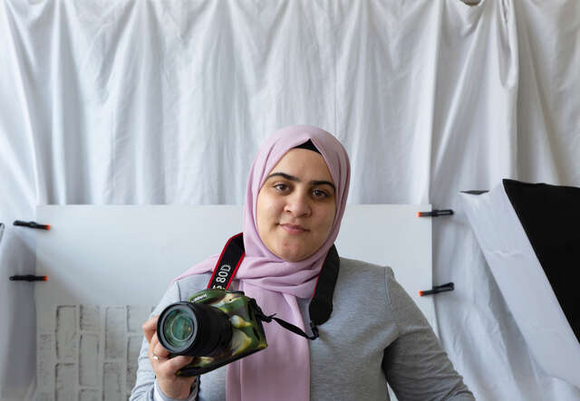 Hamida smiles, holding her camera in her hand.