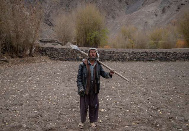 Ein Bauer steht mit einer Schaufel über der Schulter mitten auf seinem Kartoffelacker in Afghanistan.