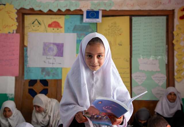 Ein Mädchen posiert für ein Foto und lächelt in einem Klassenzimmer in Afghanistan.