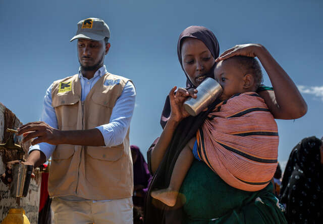 Ein Mann in einem humanitären Einsatz und eine Frau, die ein kleines Kind auf dem Rücken trägt.
