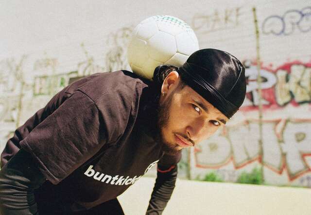 Ein junger Mann balanciert einen Fußball auf seinem Nacken vor einer mit Graffiti bedeckten Wand.