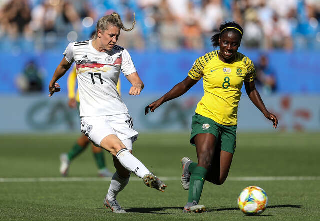 Zwei Fußballspielerinnen, eine in einem weißen Trikot und die andere in einem gelben Trikot, kämpfen während eines Spiels um den Ball.