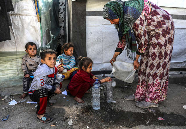 En kvinna i Gaza fyller vatten i flaskor. Barn sitter på gatan.