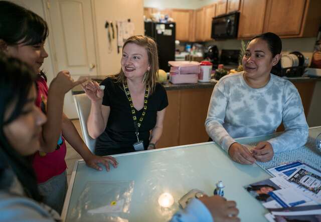 An IRC staff member sits down with a family at their kitchen table.