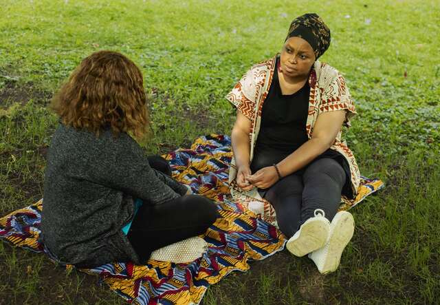Zwei Frauen sitzen auf einer Decke im Park und unterhalten sich.
