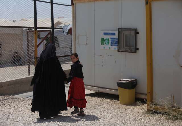 Ruba holds her mother's hands as they walk through the refugee camp they live in.