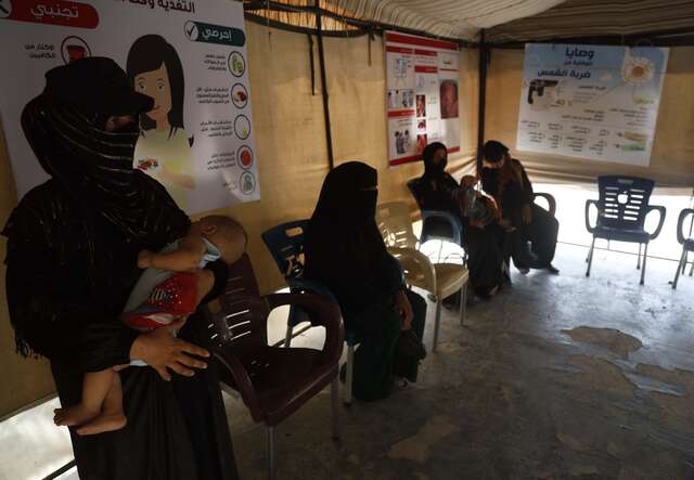 A group of women sit together in the waiting room of an IRC health centre.