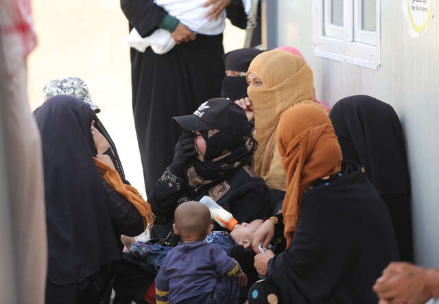 A group of women huddle around as a child is fed at the IRC health centre.