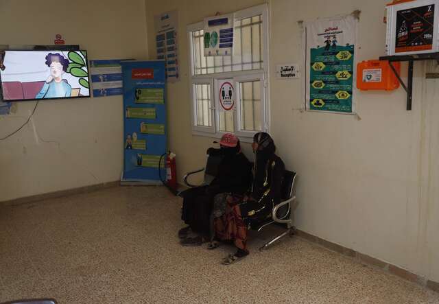 Two woman sit together in the waiting room of an IRC health center.