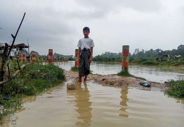 A boy stands with a soccer ball in a flooded field of the Cox's Bazaar refugee camp.