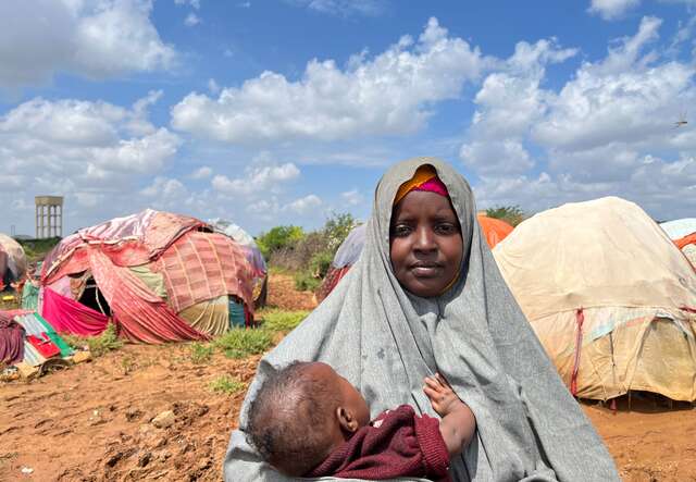 A woman holds a young child in her arms outside of their makeshift home in Somalia.