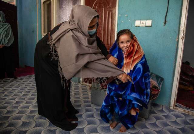 Außerhalb ihres Hauses in Kabul, Afghanistan, wickelt eine Mutter ihre lächelnde Tochter in eine neue Decke.