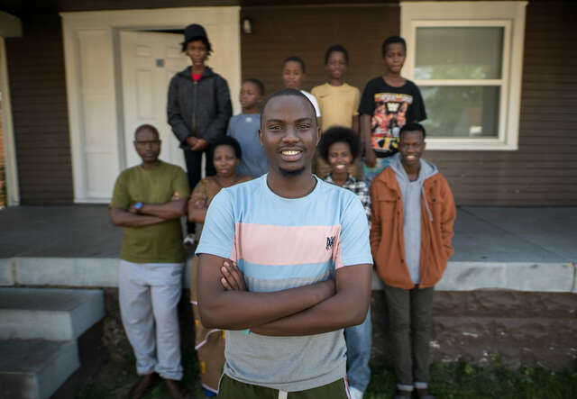 The family stand in front of their house, smiling.