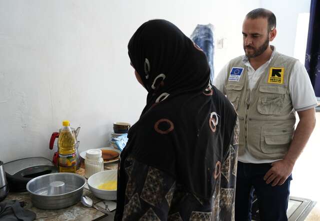 An IRC staff member stands beside an IRC client who is cooking.