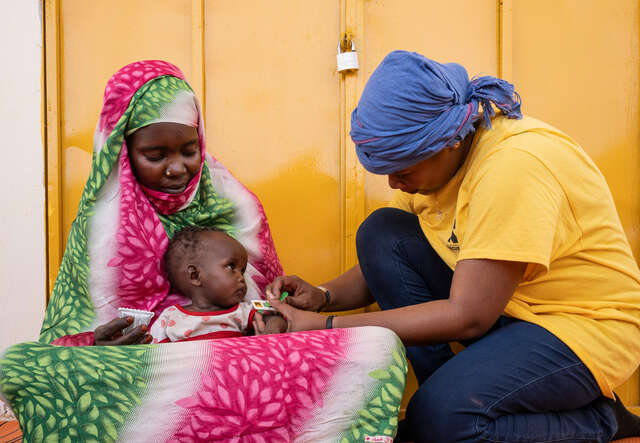 Mamma med litet barn i knäet som undersöks för undernäring av RESCUE:s personal på ett hälsocenter i Tchad.