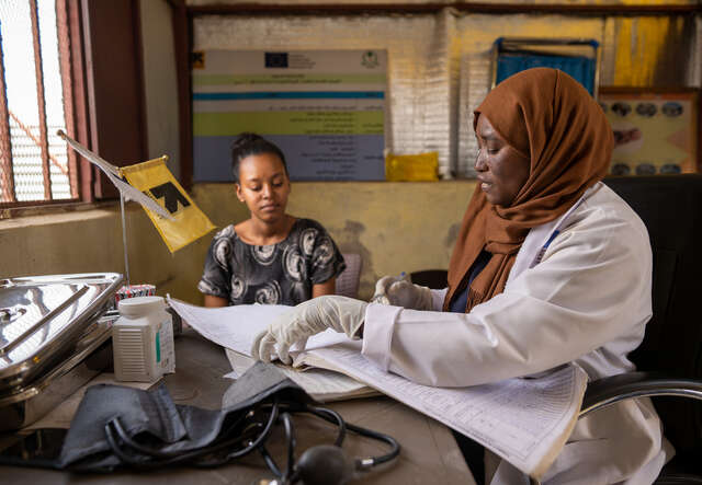 En barnmorska på RESCUE:s klinik i Sudan sitter vid ett bord bredvid en kvinnlig patient.