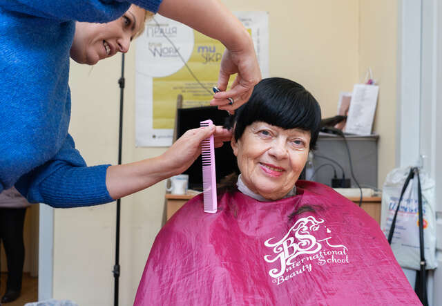 Eine Frau in der Ukraine sitzt auf einem Friseurstuhl und wird von einer anderen Frau die Haare geschnitten.