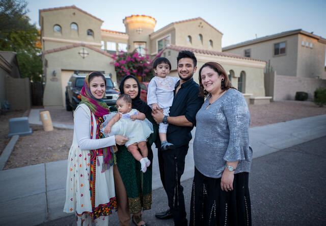 A family, 4 adults and two small children, stand in front of their home in Arizona. 