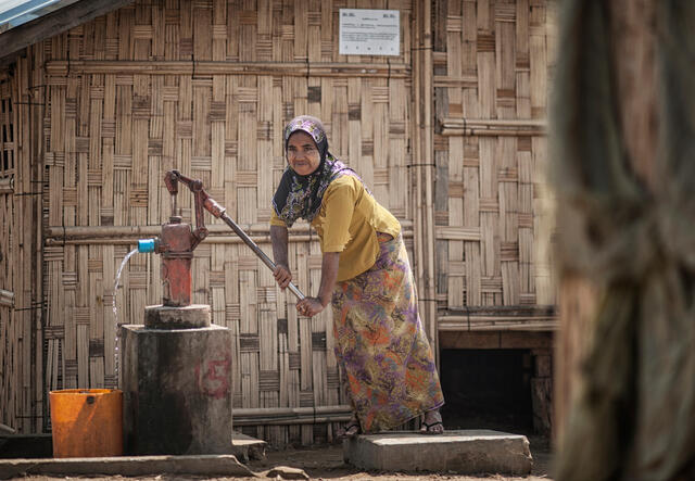 A woman uses a hand pump to draw water from a well in a displacement camp.