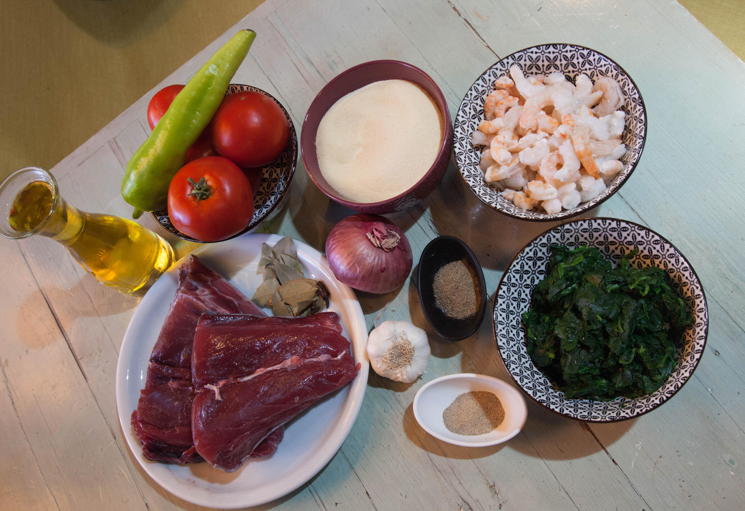 Raw tuna, tomatoes, spinach, garlic, onions, and other ingredients laid out on a table.