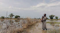 Abuk, holding Nyirou, poses for a portrait in front of their flooded house, in Northern Bahr El Ghazal, South Sudan.