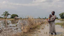 A mother holds her daughter tight to her chest while walking outdoors in a flooded region of South Sudan.