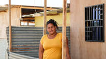A woman stands outside a makeshift shelter and poses for a photo.