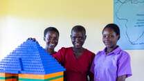 Three students smile and pose for a photo in a school in Uganda.