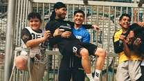 Eine Gruppe von Kindern posiert lachend in einem Fußballtor, wobei einige von ihnen andere Kinder auf den Armen tragen.