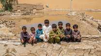 8 boys sit together outside in Pakistan, in front of a landscape devastated by flooding.