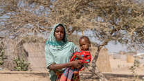 A mother holds her daughter and the pair poses for a photo outside of a home in Chad.