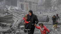 A mother holds her two children while she makes her way through the remnants of a building destroyed by the war in Gaza.
