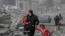 A mother holds her two children while she makes her way through the remnants of a building destroyed by the war in Gaza.